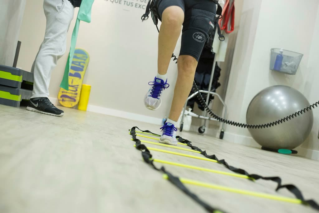 Patient in a knee brace doing agility-ladder exercises with a physiotherapist